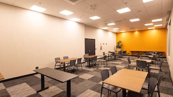 Sala de conferências com várias mesas e cadeiras, piso coberto por carpete e uma parede amarela como detalhe.