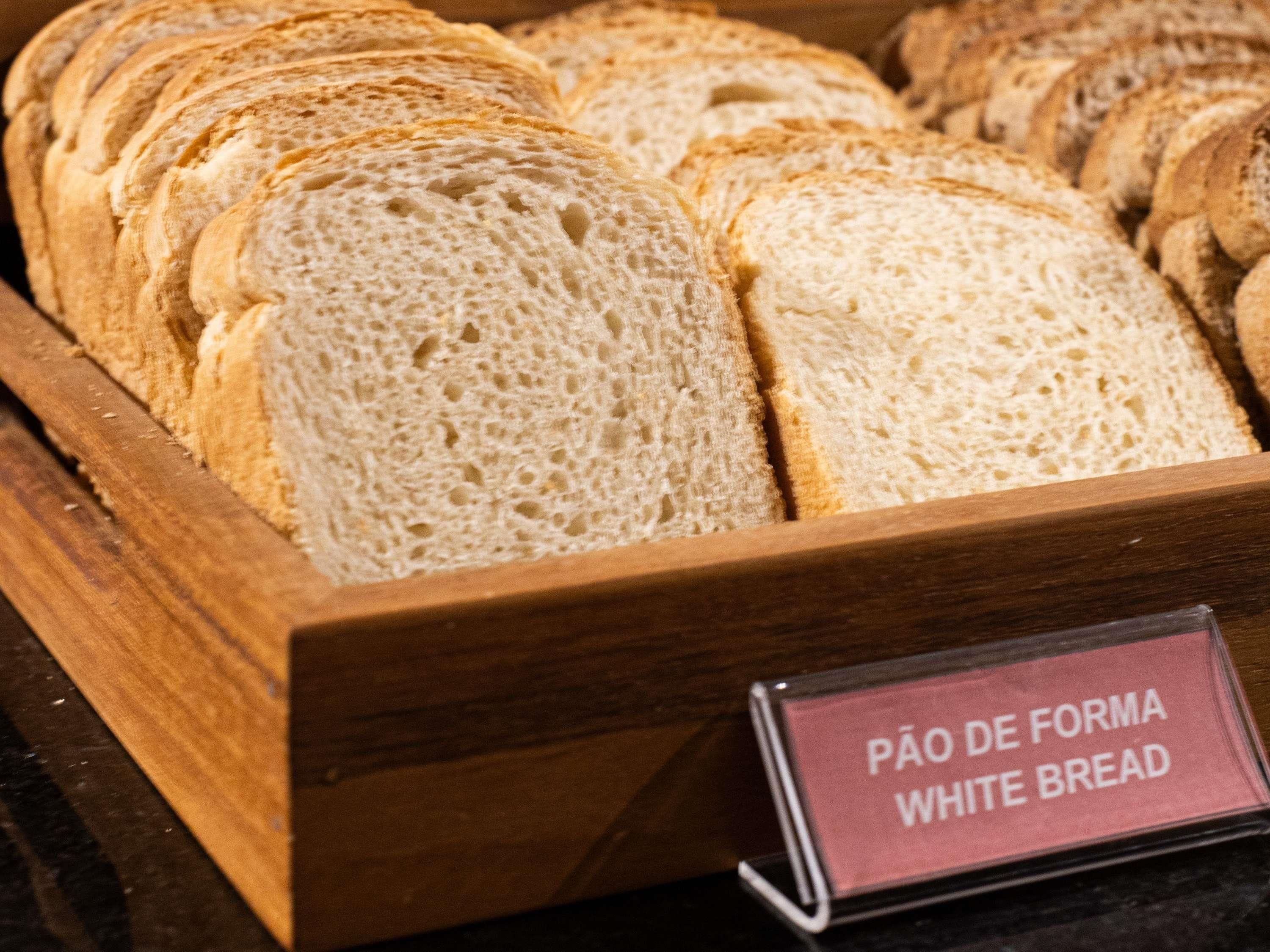 Una vitrina de madera con rebanadas de pan blanco, identificadas con la etiqueta 'Pão de Forma White Bread'.