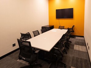 A conference room with a long table, chairs, a flat-screen TV mounted on the wall, and carpeted flooring. - Ibis Barra Do Garcas (Barra do Garcas)