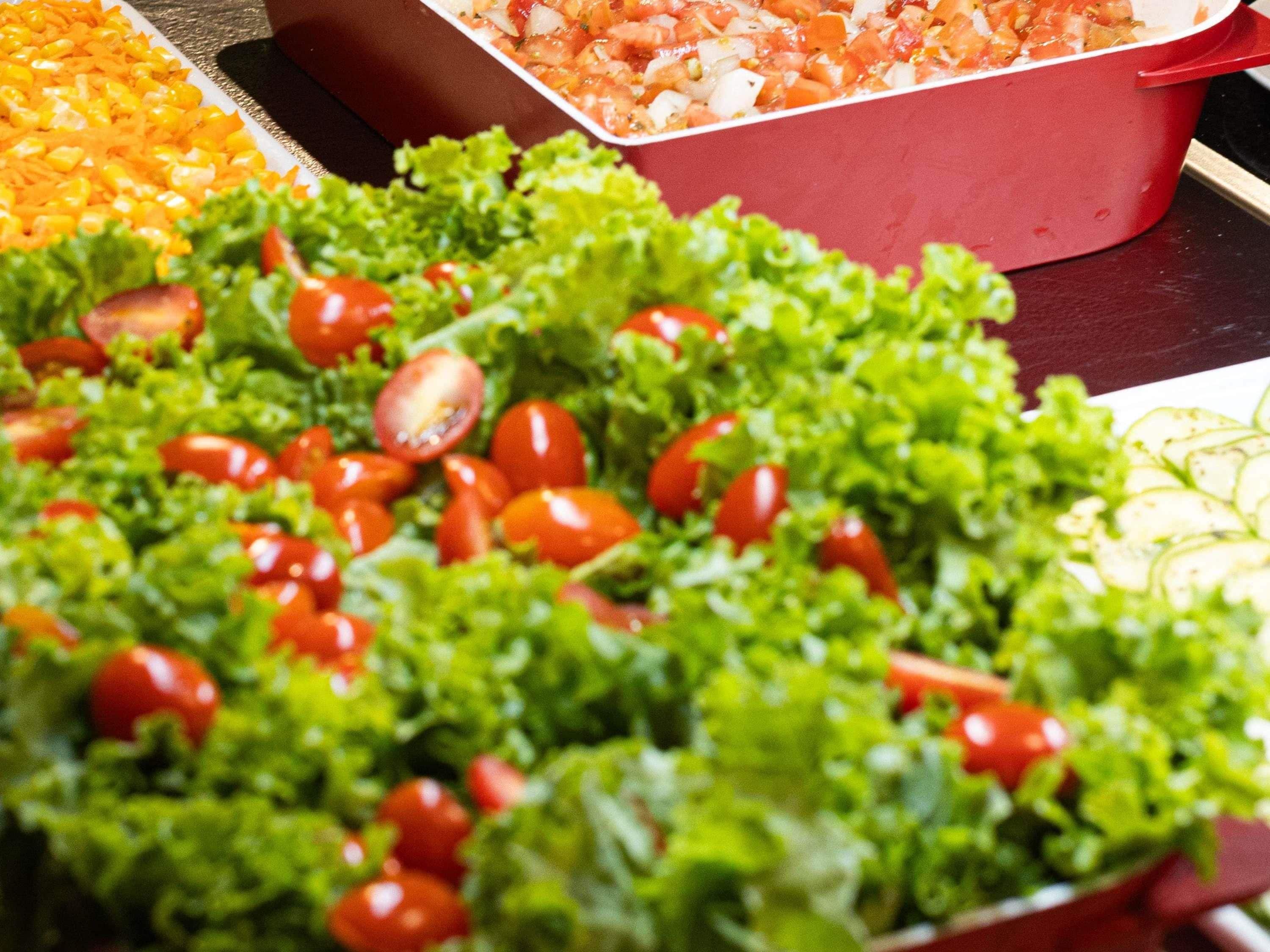A buffet table with various dishes including a salad with lettuce and cherry tomatoes, a container of diced tomatoes, and a dish with corn.
