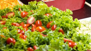 A buffet table with various dishes including a salad with lettuce and cherry tomatoes, a container of diced tomatoes, and a dish with corn.