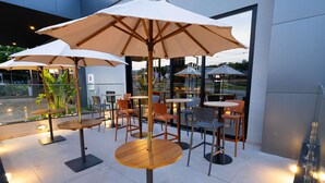 Outdoor seating with tables and chairs, umbrellas, and a building in the background. - Ibis Barra Do Garcas (Barra do Garcas)