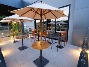 Outdoor seating with tables and chairs, umbrellas, and a building in the background. - Ibis Barra Do Garcas (Barra do Garcas)