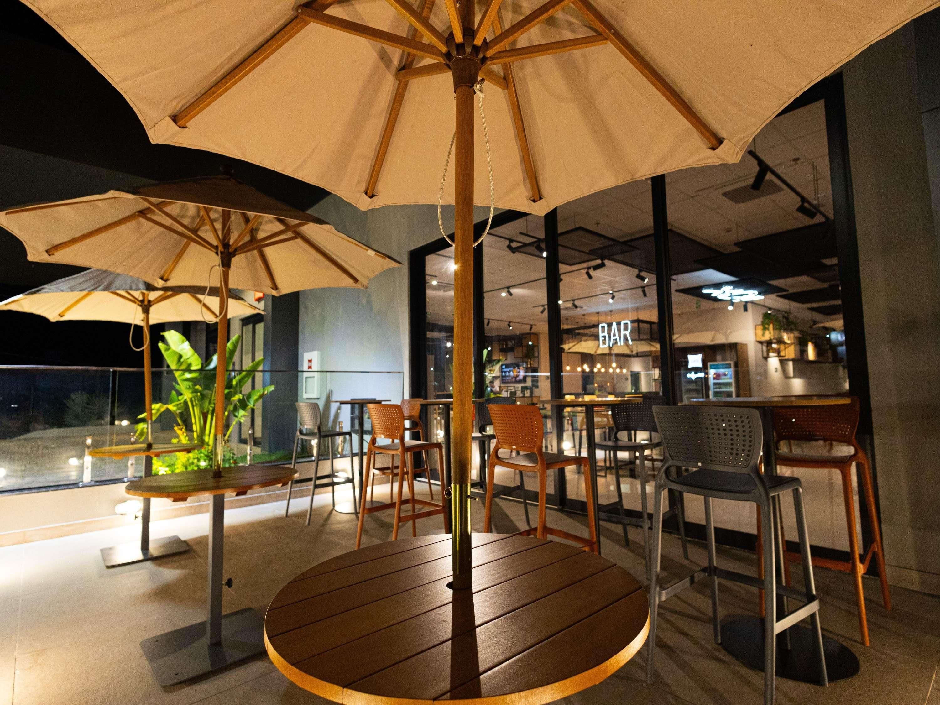 A restaurant with outdoor seating, including round tables and chairs, under large umbrellas.