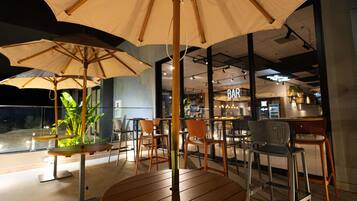 A restaurant with outdoor seating, including round tables and chairs, under large umbrellas.