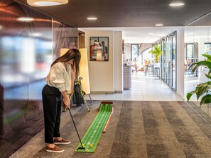 En person som spelar golf inomhus, med en puttinggreen och en golfbag.