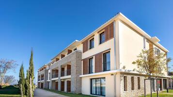 A multi-story residential building with balconies, large windows, and a well-maintained lawn.