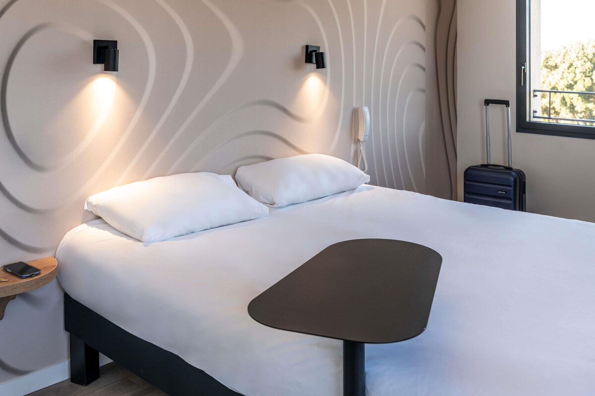A modern hotel room with a bed, bedside table, and a suitcase.