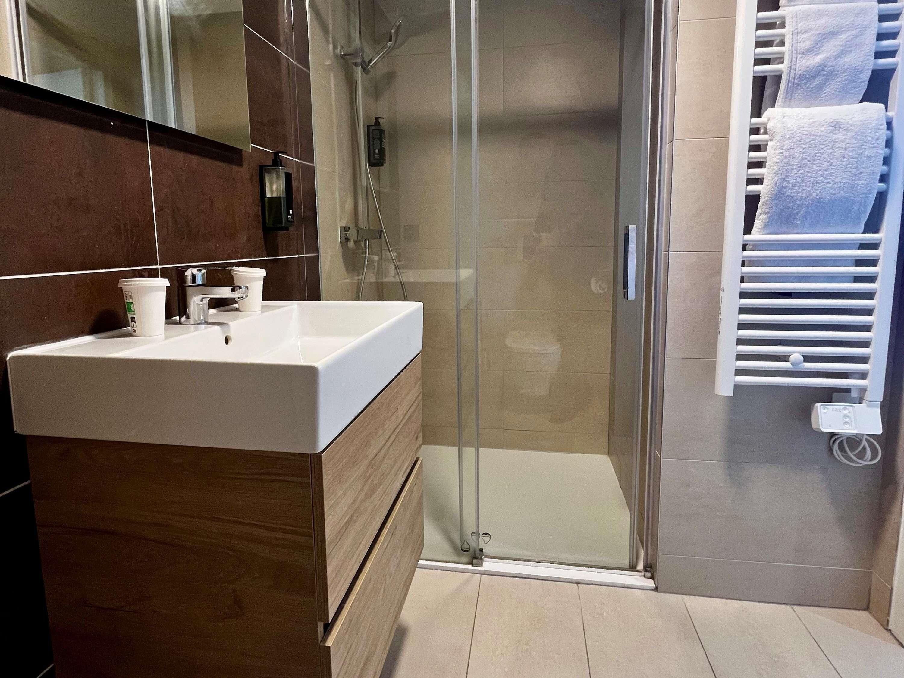 Un bany modern amb una dutxa de vidre, un lavabo blanc i un escurapulides.