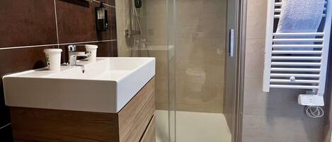 Un bany modern amb una dutxa de vidre, un lavabo blanc i un escurapulides.