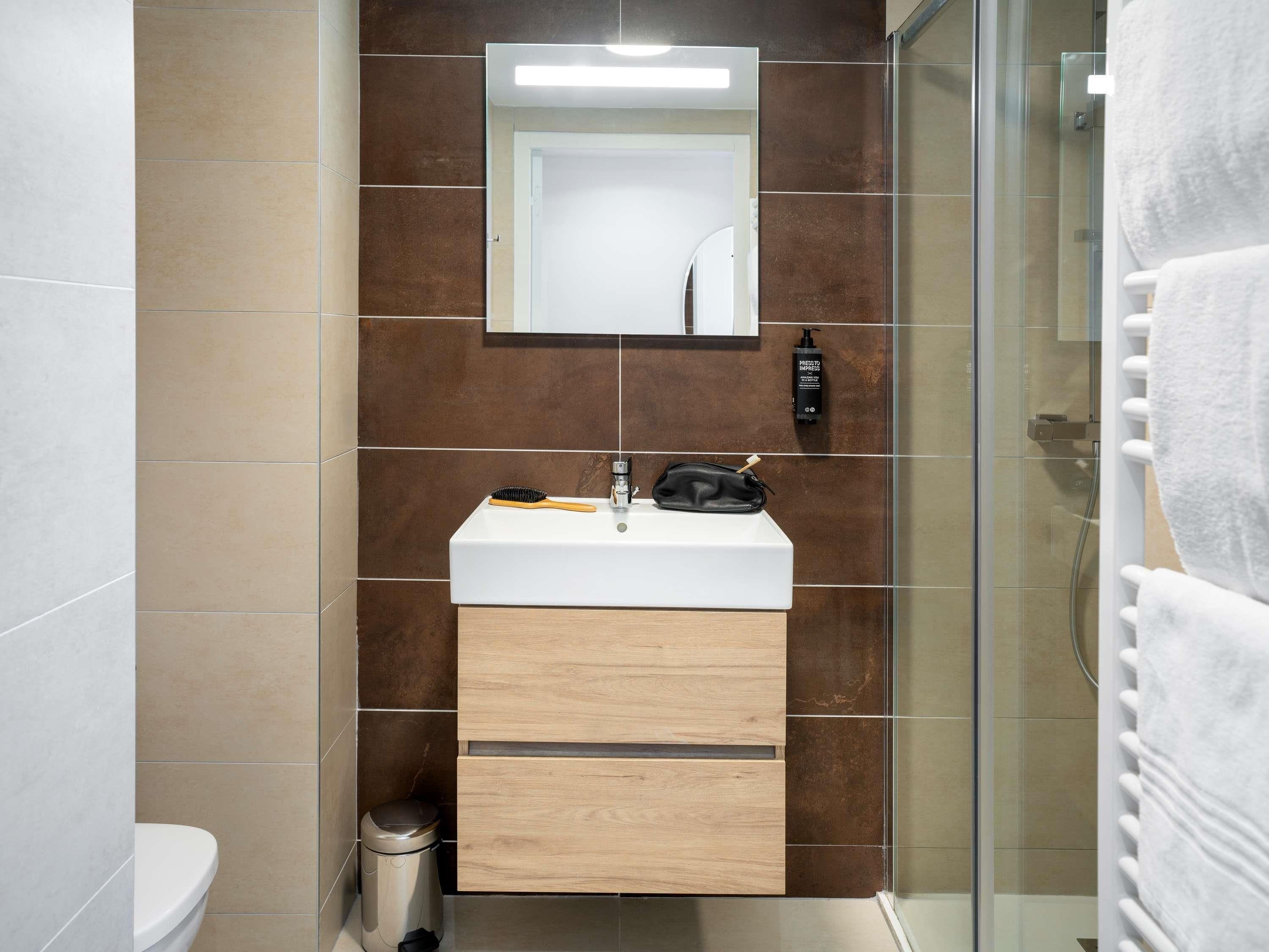 Un baño con lavamanos blanco, mueble de madera y cabina de ducha de vidrio.