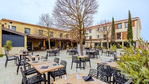 An outdoor café with multiple tables and chairs, surrounded by buildings with a yellow facade and red-tiled roofs. - Ibis Styles Cabriès Aix-En-Provence Tgv  (Cabries)