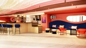 A modern bar area with a wooden counter, blue bar stools, and a seating area with red chairs and a blue sofa. - Ibis Styles Cabriès Aix-En-Provence Tgv  (Cabries)