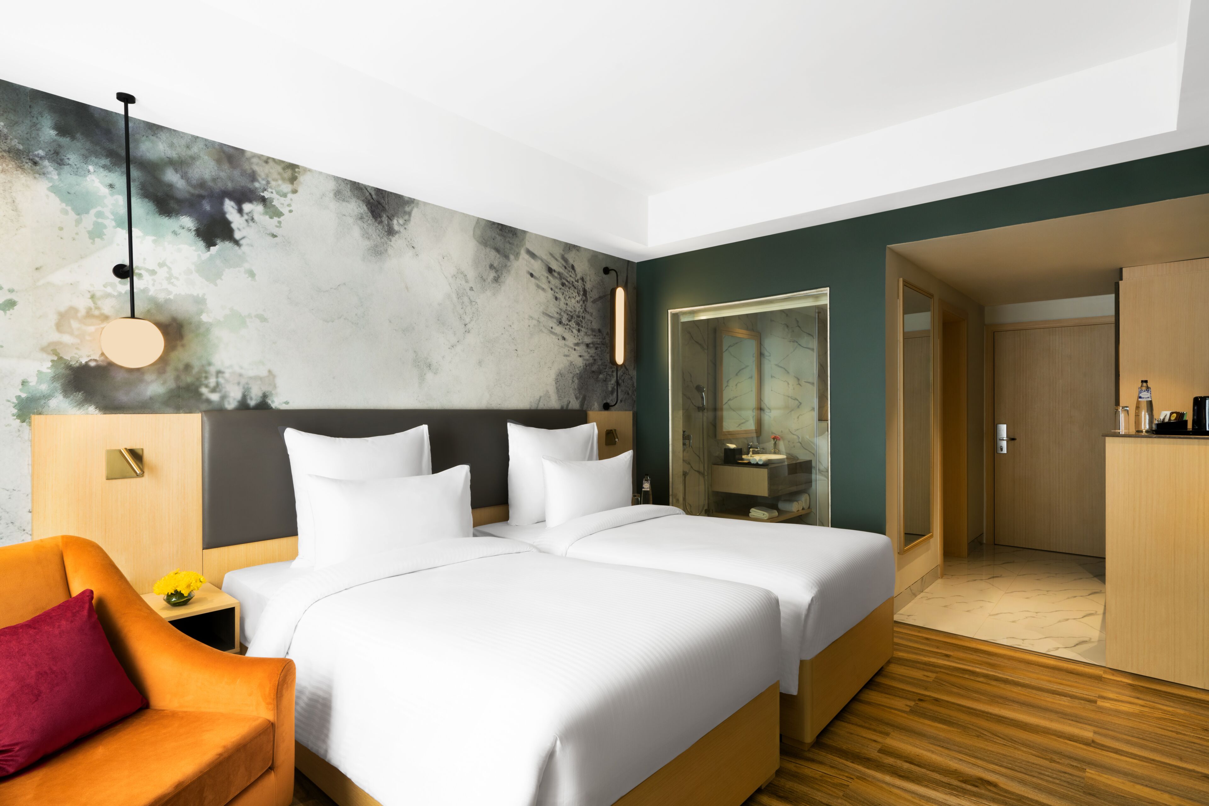 A hotel room with a large bed, a nightstand, a chair, a bathroom with a mirror, and a wooden wardrobe.
