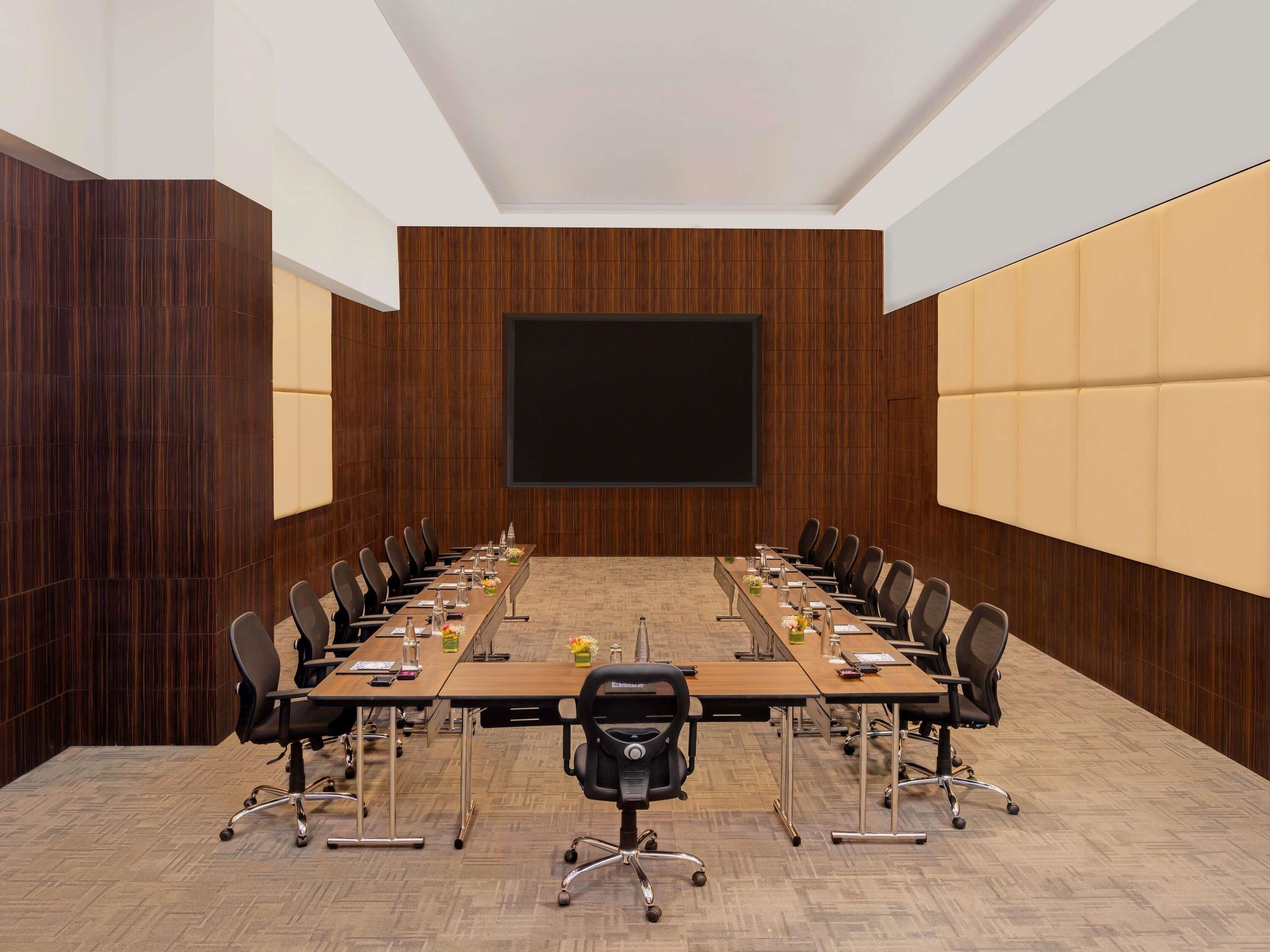 A conference room with a long table, chairs, a projector screen, and wooden paneling.