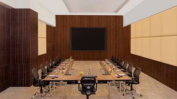 A conference room with a long table, chairs, a projector screen, and wooden paneling.