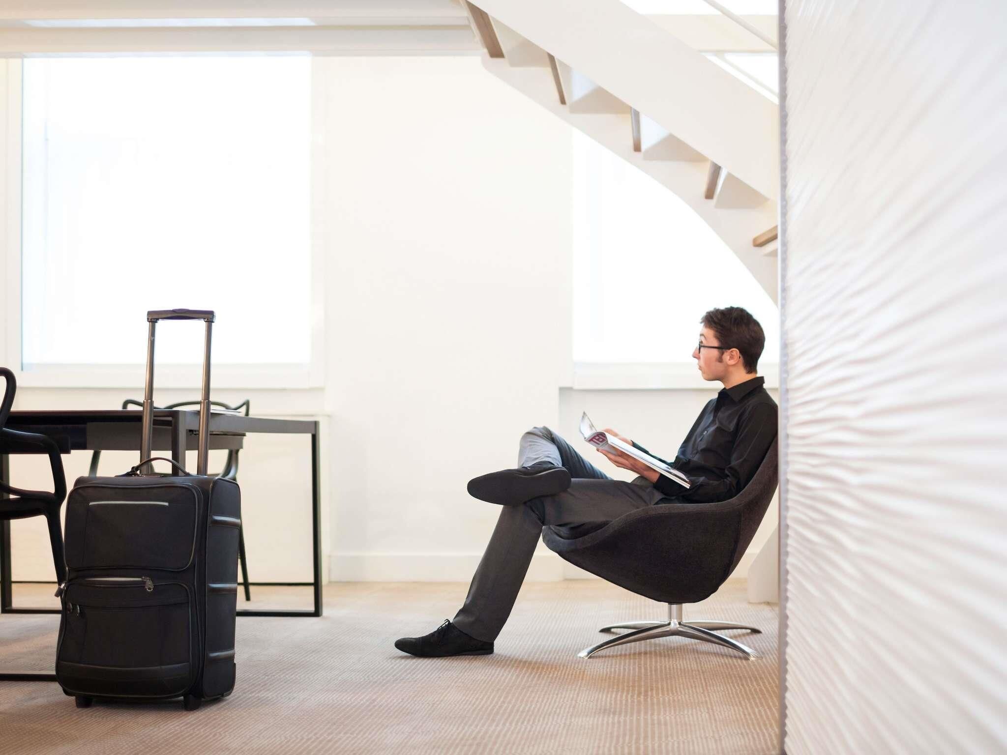 Una habitación de hotel moderna con un ventanal grande, una escalera y un rincón de descanso con una silla y una maleta.
