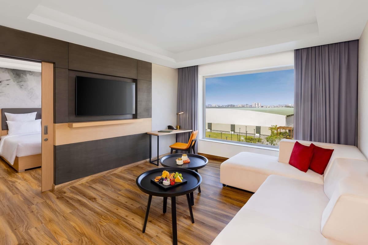 Een moderne hotelkamer met een groot bed, een slaapbank, een aan de muur bevestigde televisie en een eettafel met uitzicht op de stad.