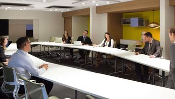 Un salón de conferencias con una larga mesa, sillas e iluminación en el techo.