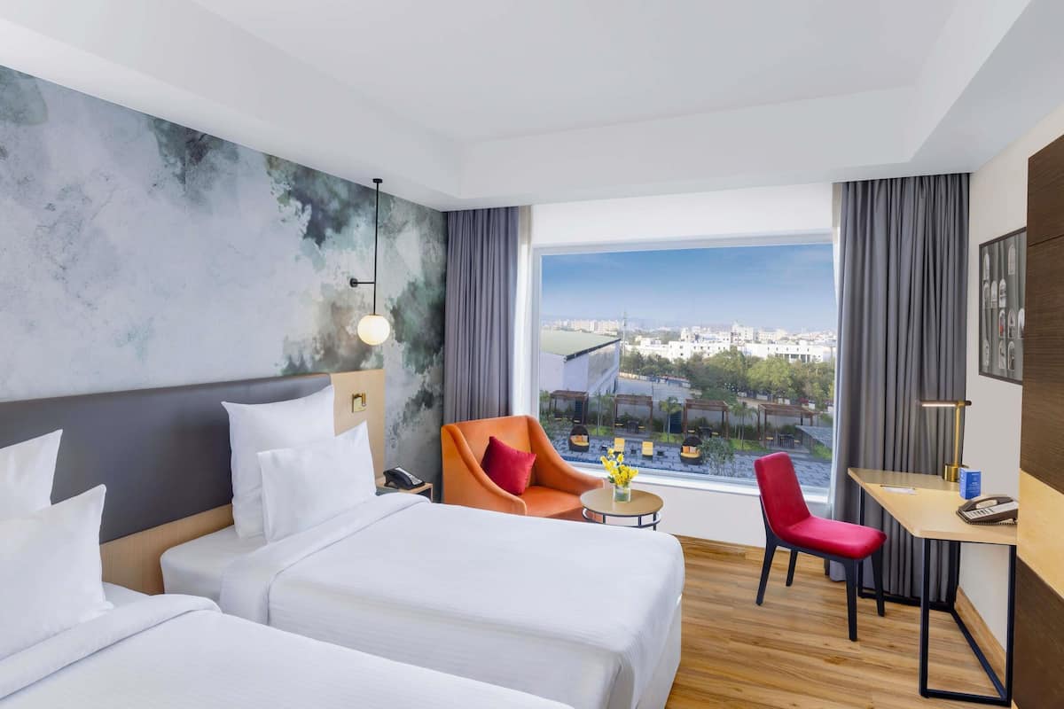 Une chambre dâhĂŽtel avec deux lits, un bureau, une chaise, une vue sur la ville et une grande fenĂȘtre.