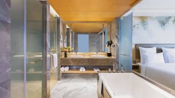 A modern bathroom with a large bathtub, two sinks, and a shower area.