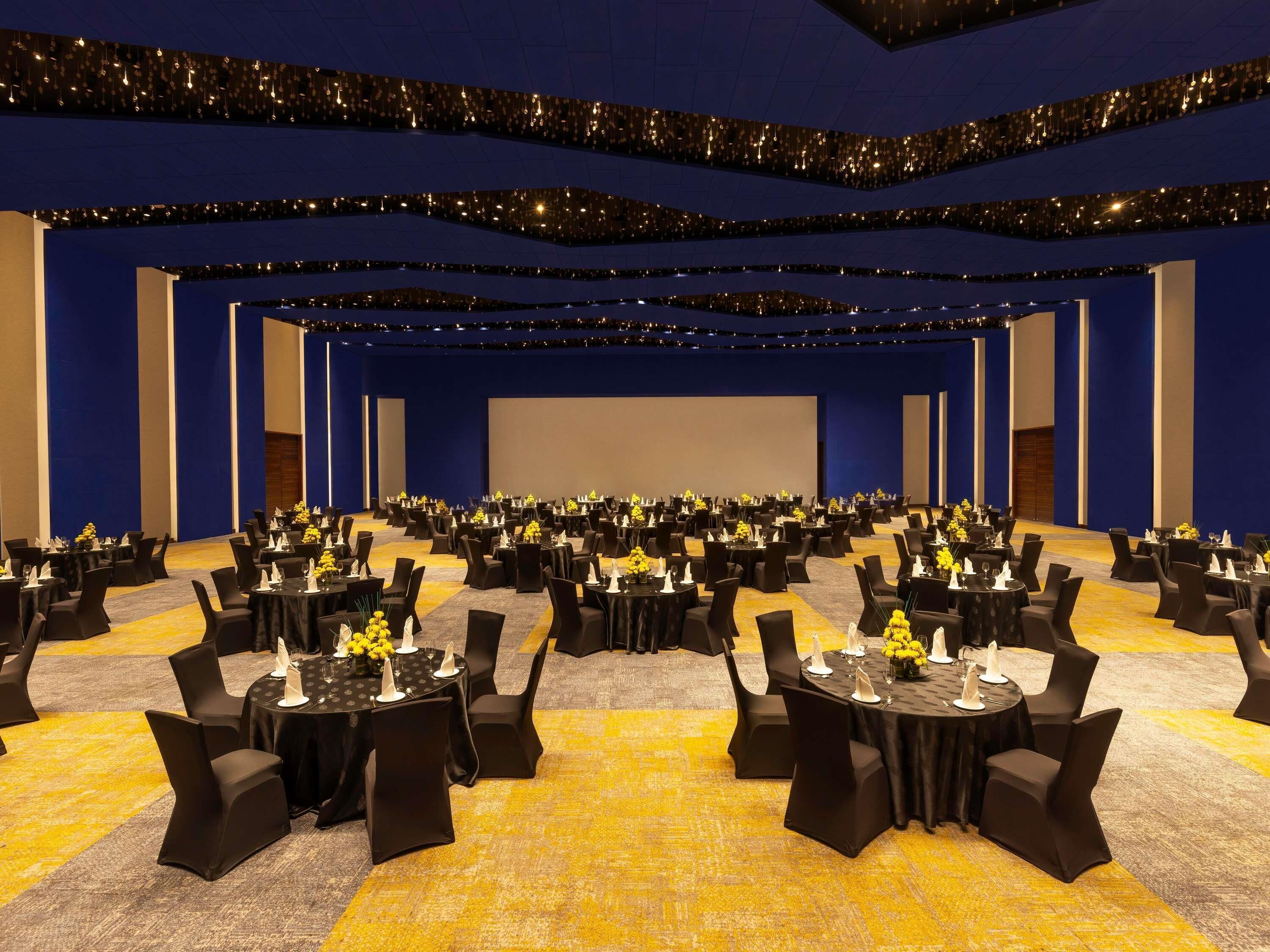 A large conference room with rows of tables and chairs, a stage, and a blue carpet.