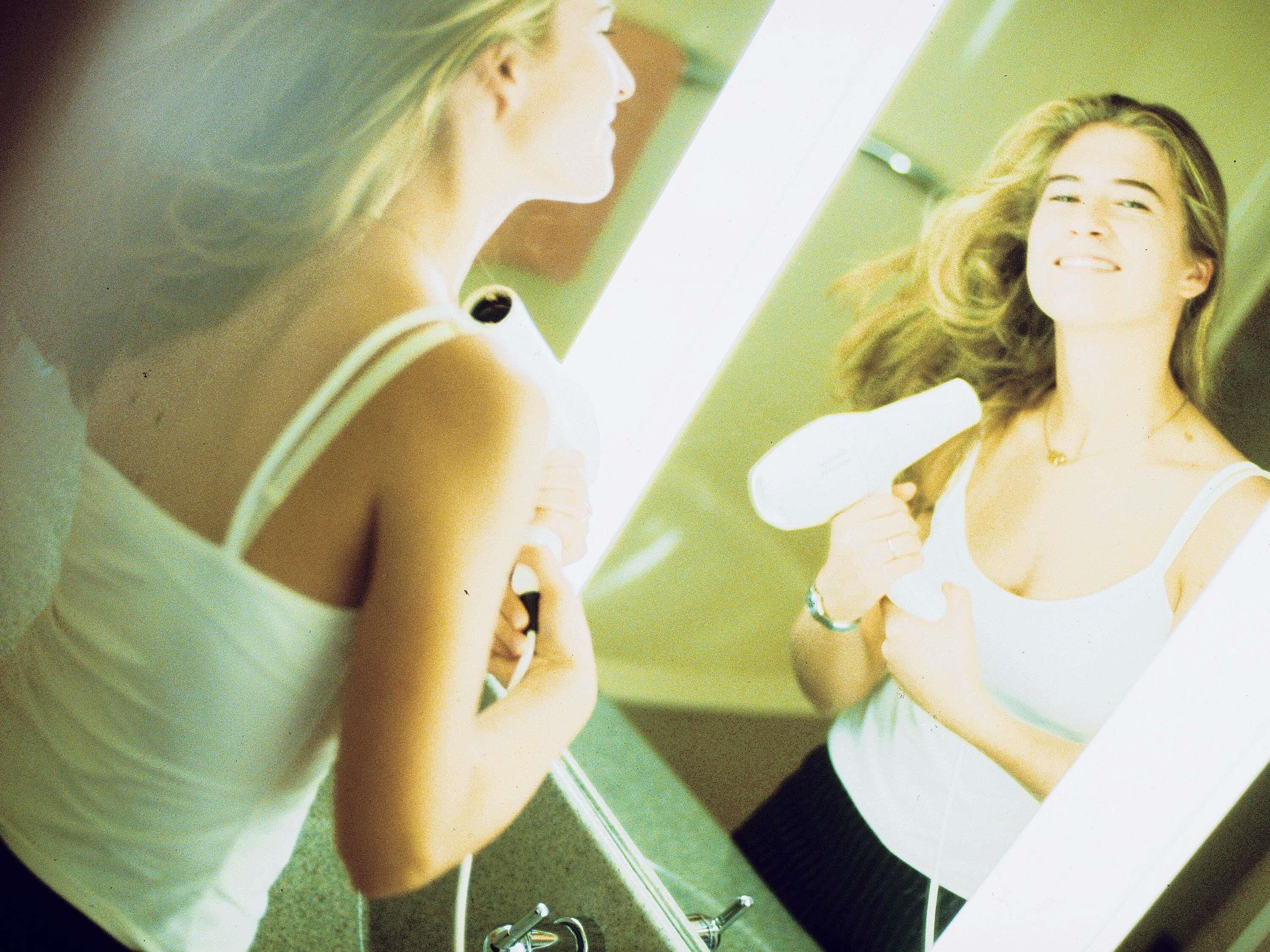 A person using a hairdryer in front of a mirror.