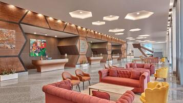A modern lobby with a reception desk, seating areas, and a staircase.