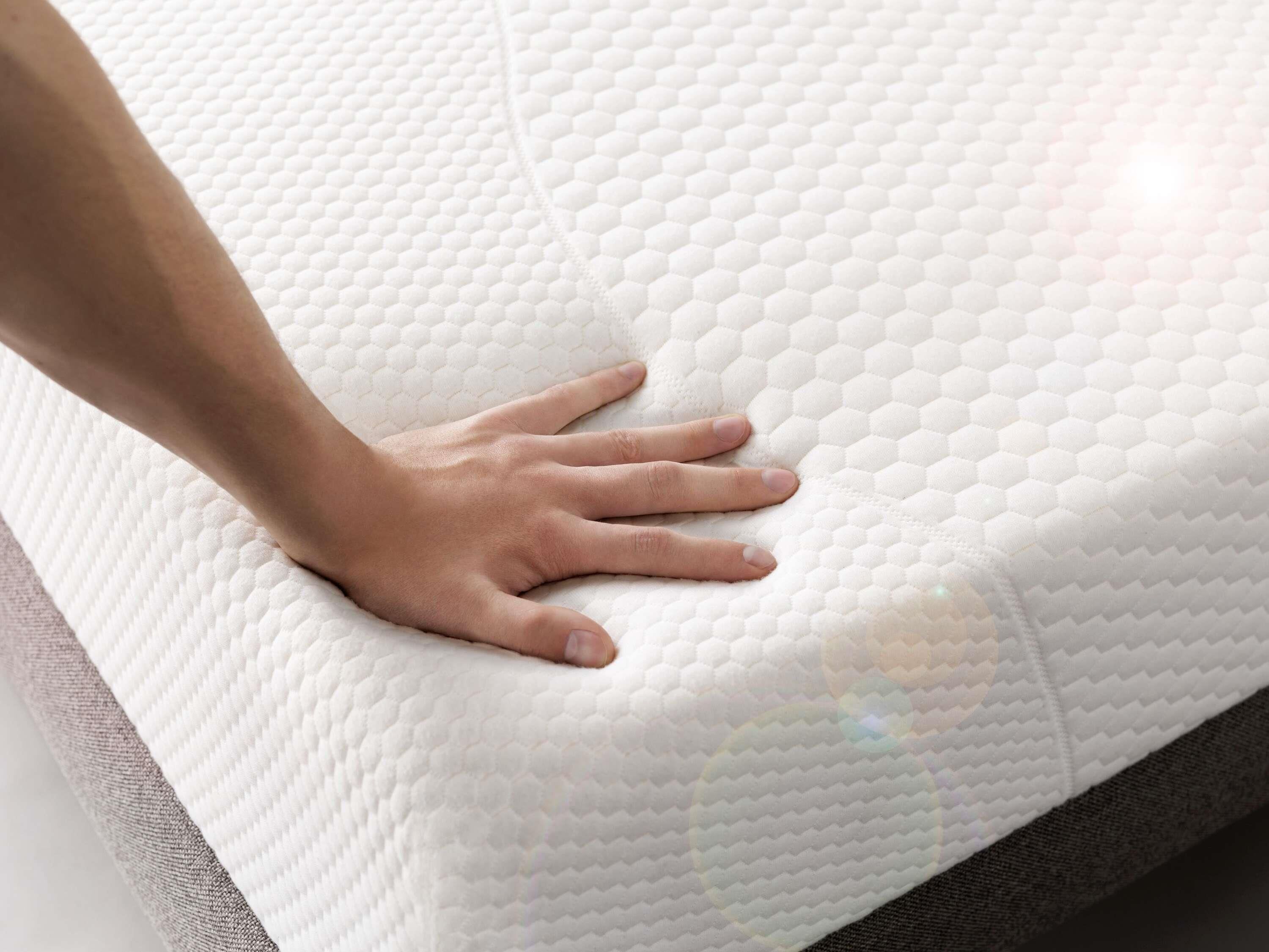 A hand resting on a white textured mattress.