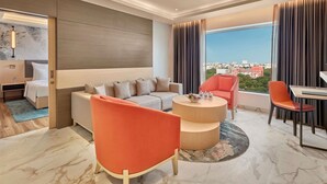 Een moderne hotelkamer met een bank, fauteuils, een eettafel en een groot raam met uitzicht over de stad.