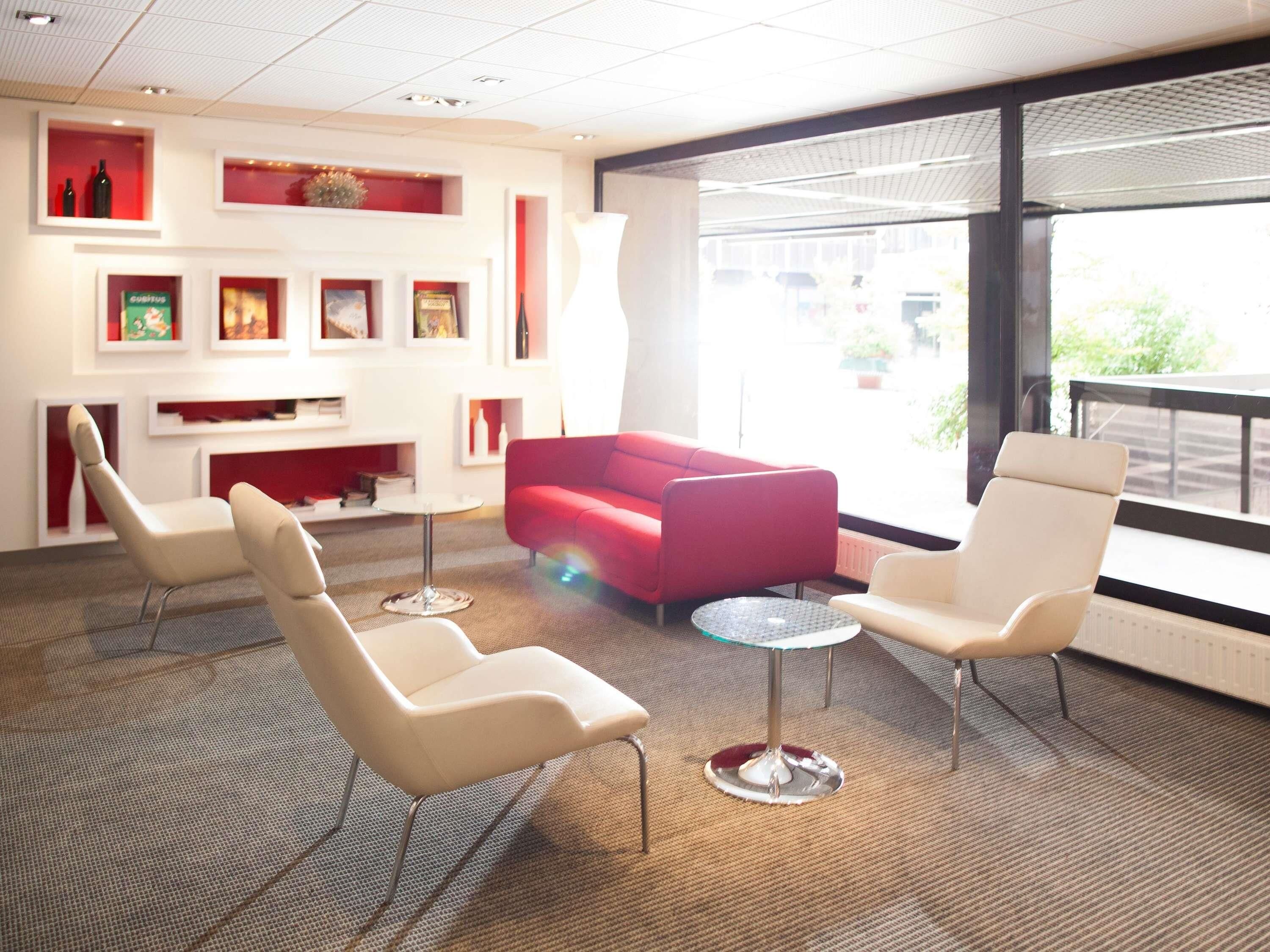 A modern interior with a red sofa, white chairs, and a glass table.