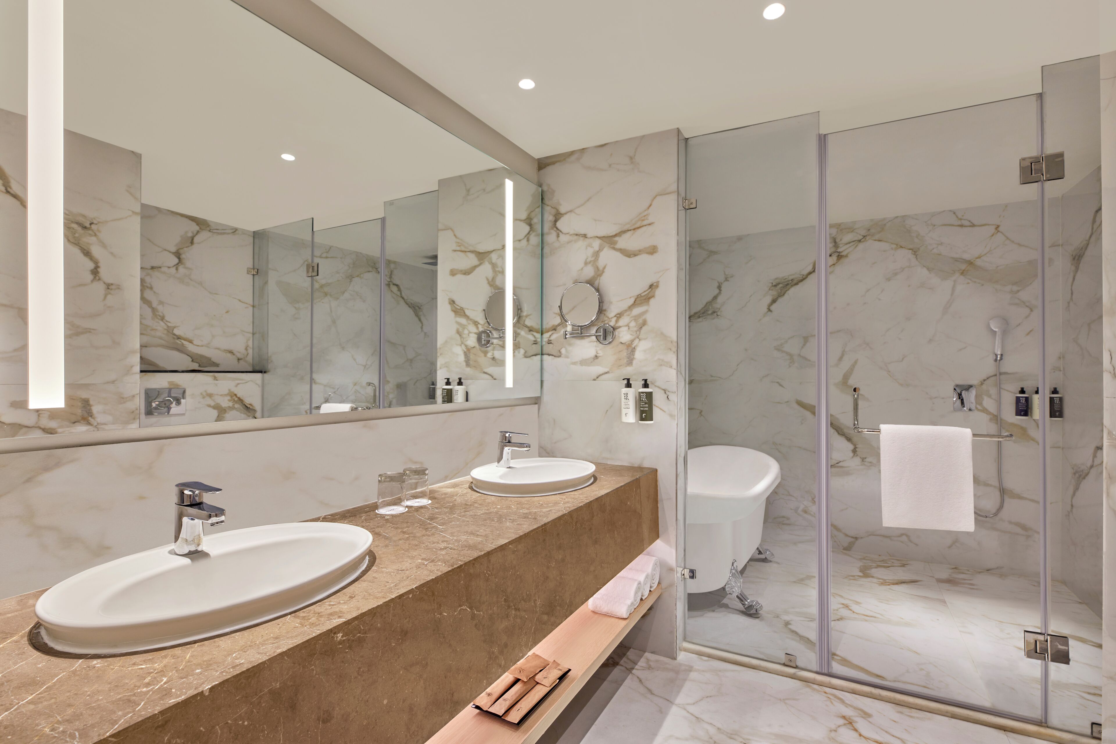 A modern bathroom with a marble vanity, dual sinks, a glass shower enclosure, and a large mirror.