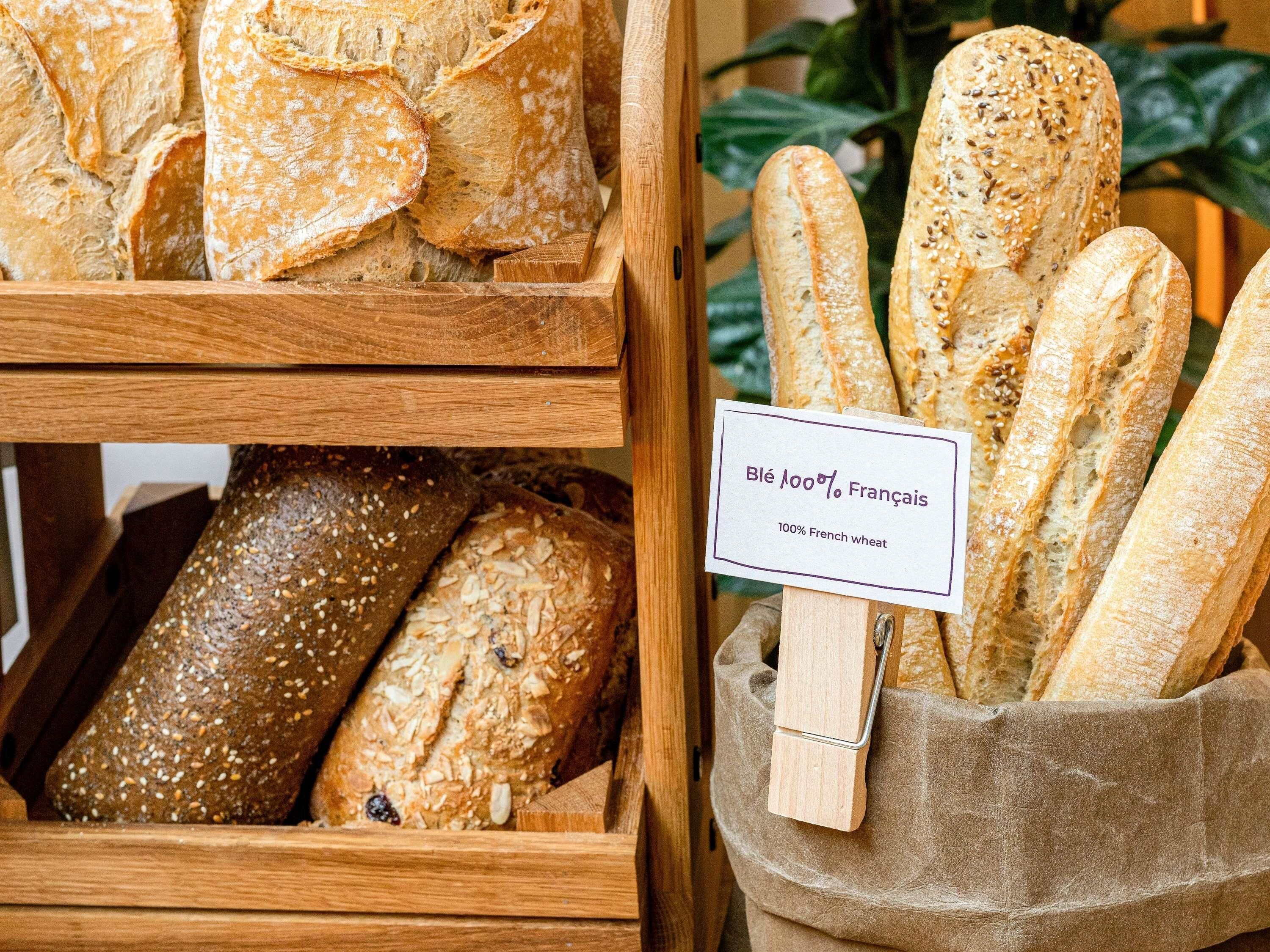 A display of various breads, including baguettes and multigrain loaves, with a sign indicating they are made from 100% French wheat.