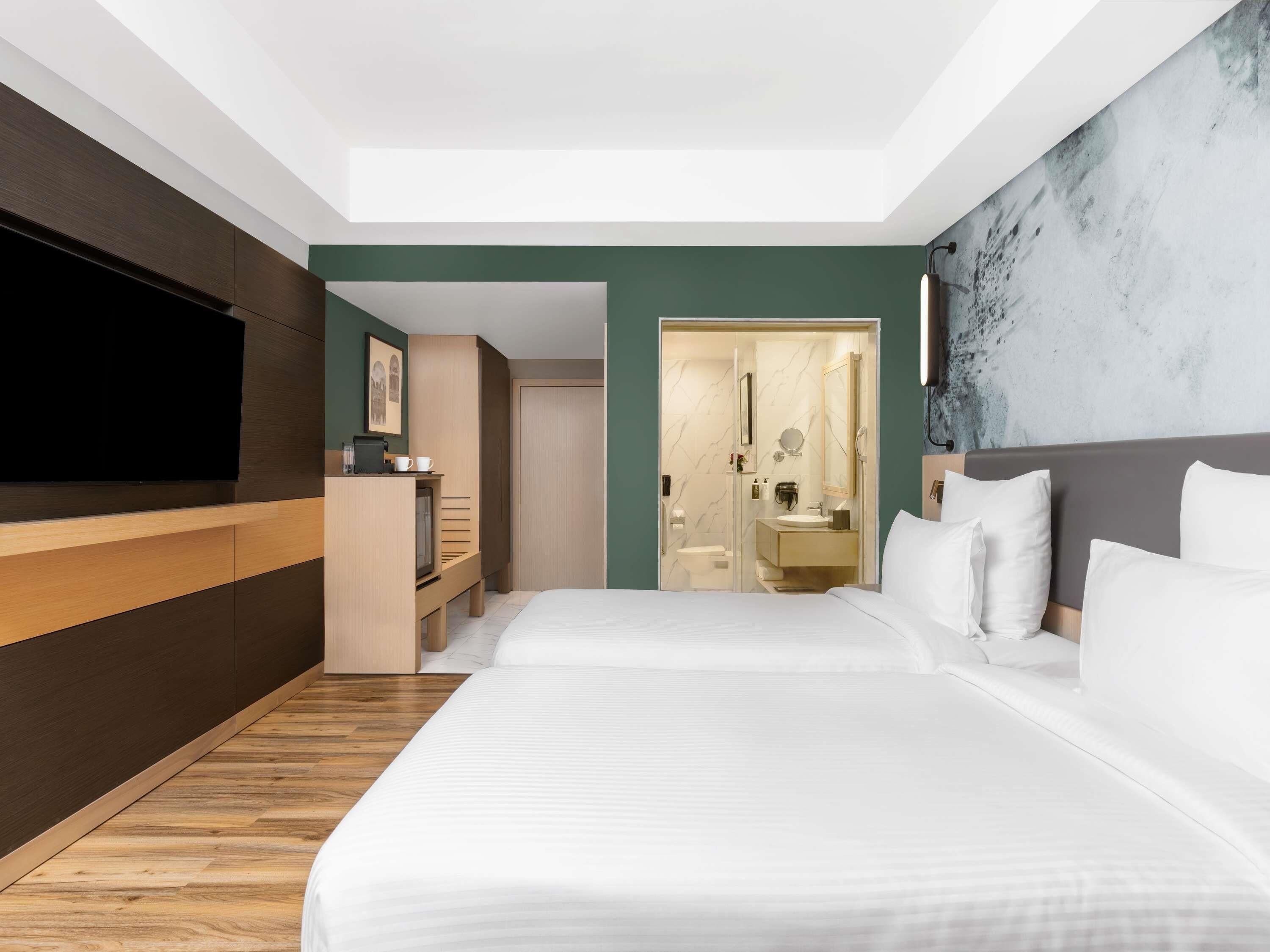 Ein modernes Hotelzimmer mit einem großen Bett, einem Fernseher, einem Schreibtisch und einem Badezimmer.