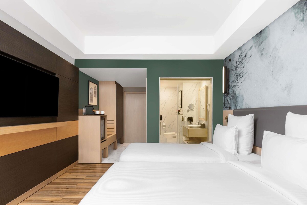 A modern hotel room with a large bed, a TV, a desk, and a bathroom.