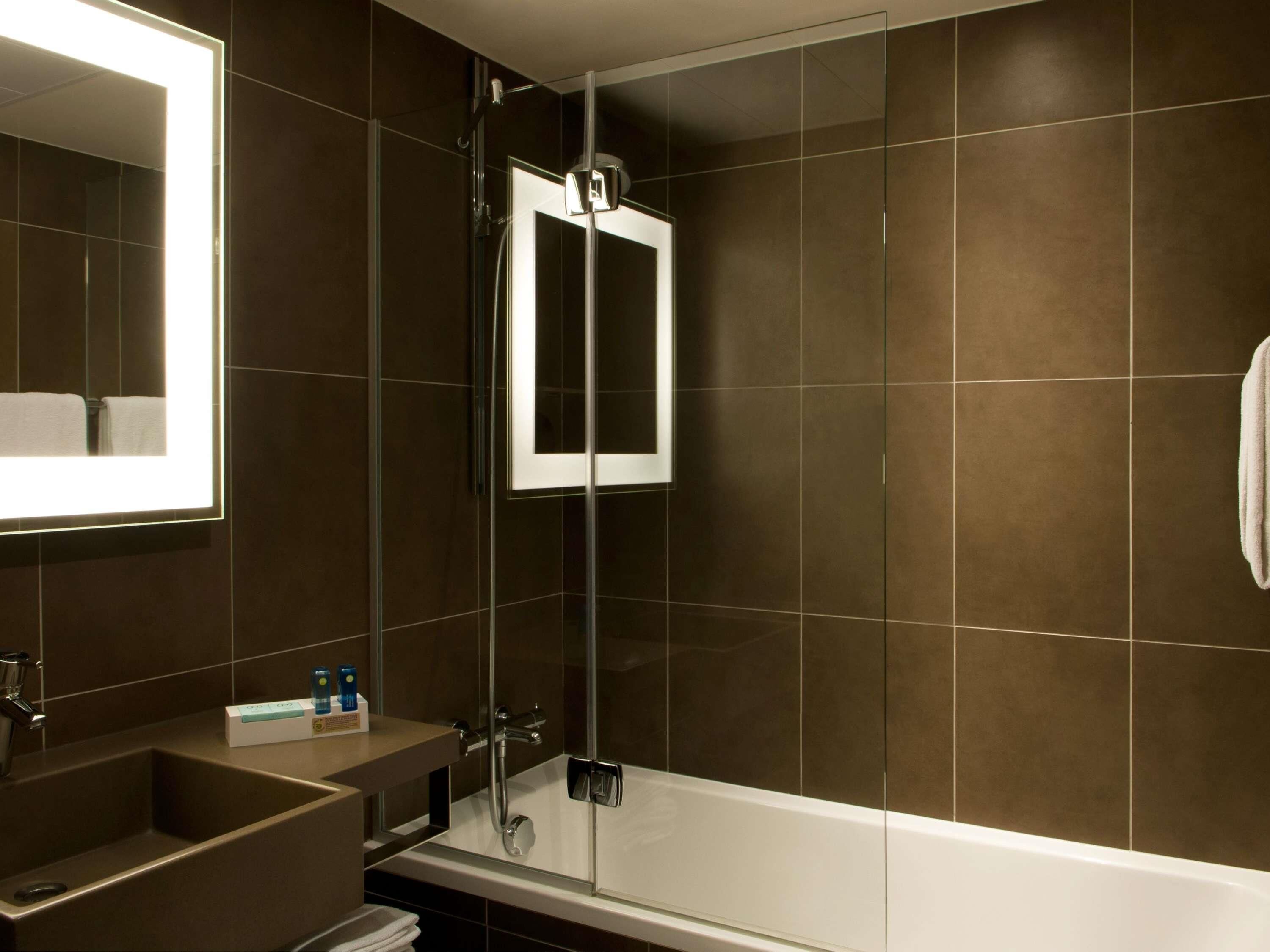 A modern bathroom with a glass-enclosed shower, a large mirror, and a bathtub.