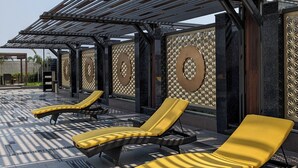 Een zonnig buitengebied met lounge fauteuils en een pergola.
