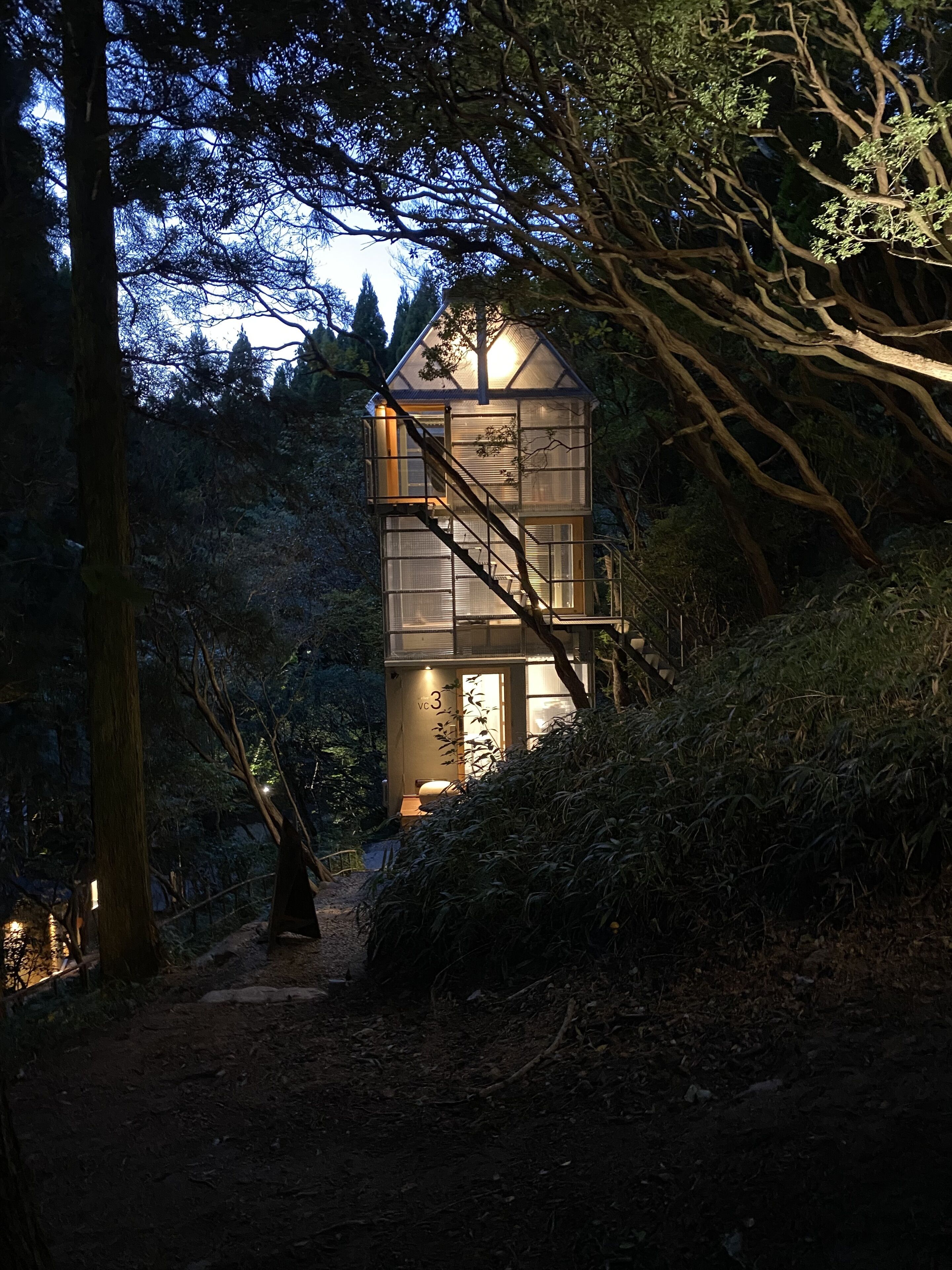 Une tour de verre avec un escalier, entourée d’arbres et bordée d’un sentier de terre.