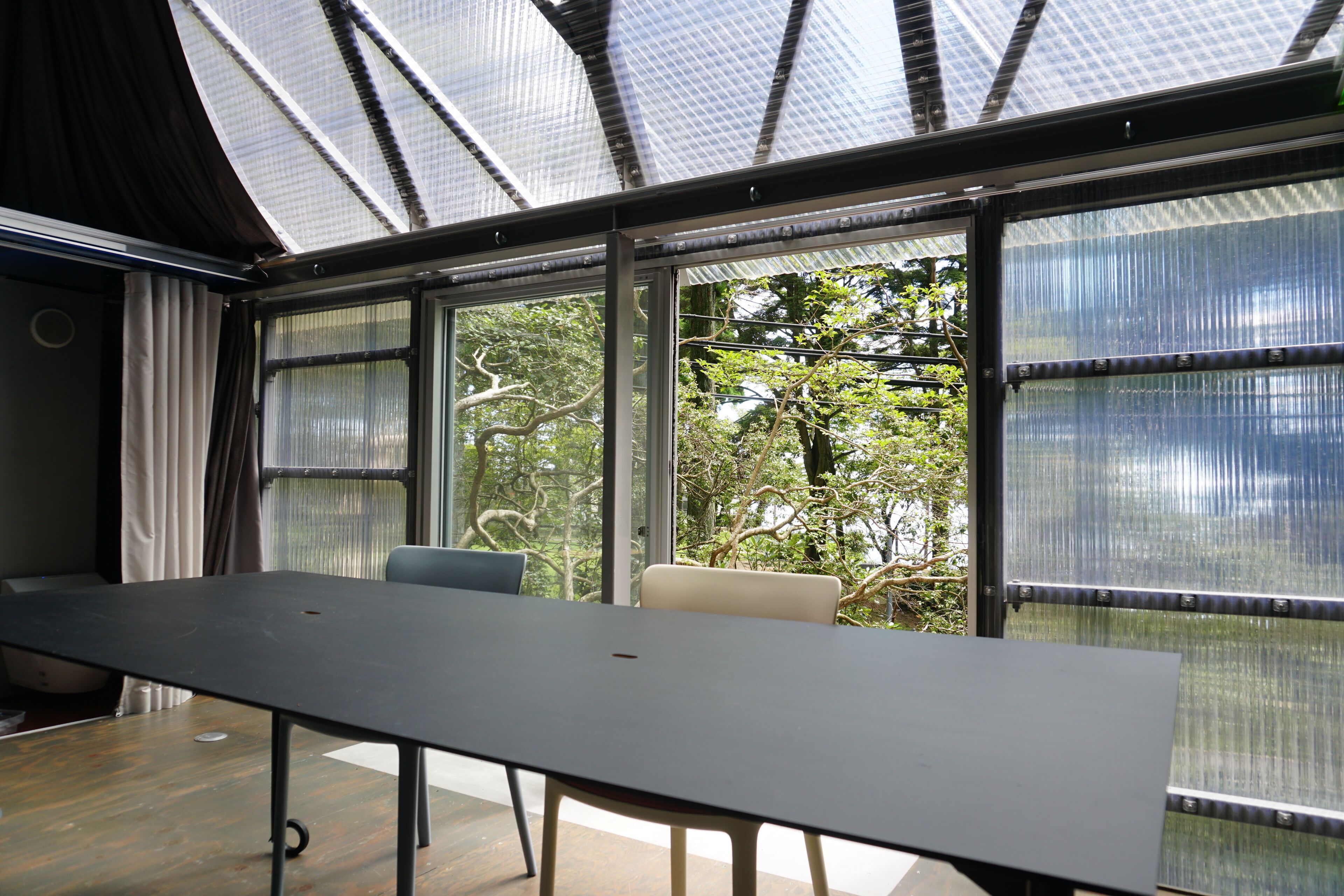 A modern room with a large table, two chairs, and large windows with a view of trees.