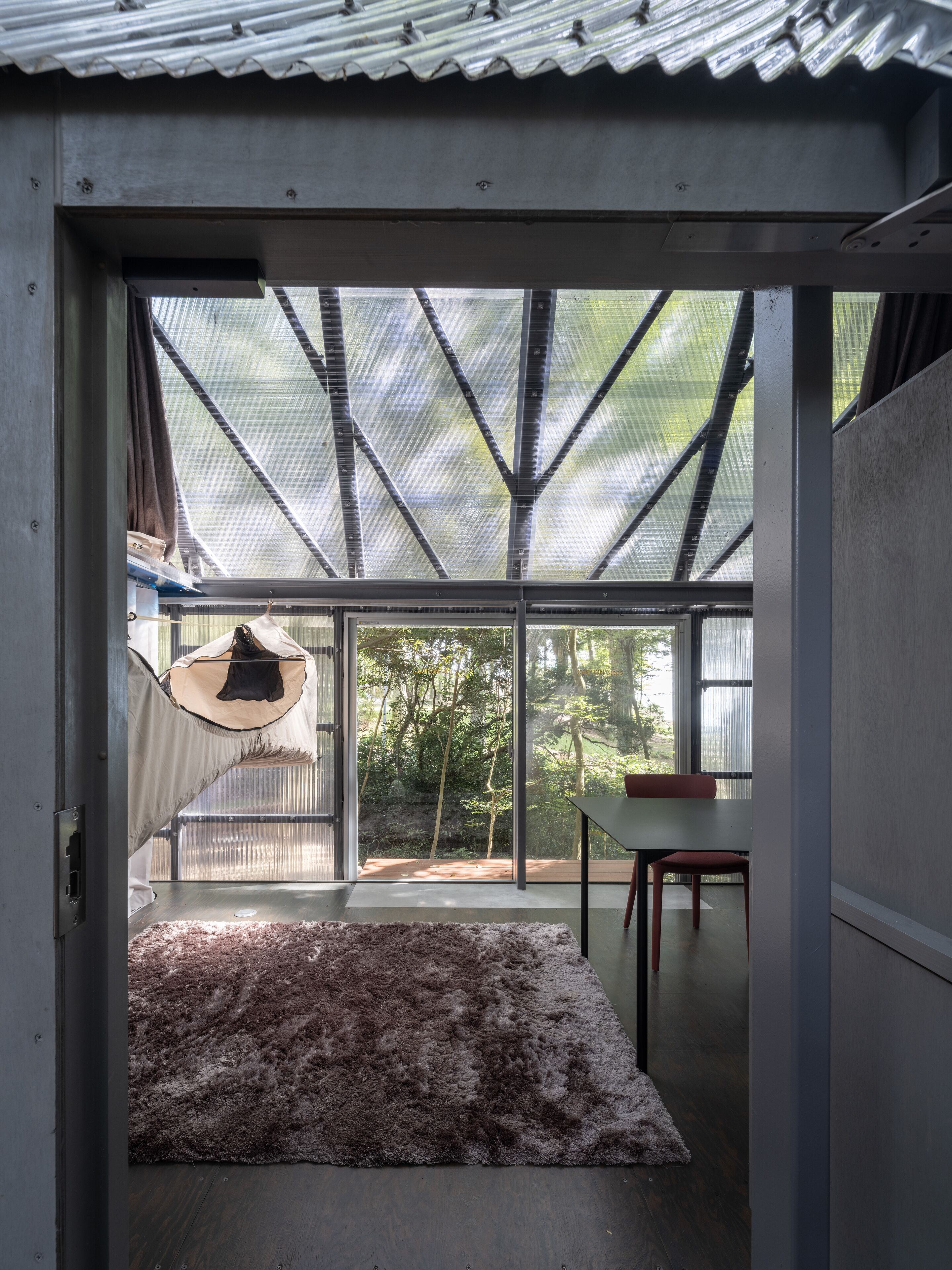 Un interior modern amb una gran porta de vidre que dona a una zona exterior, una taula de fusta i una catifa al terra.