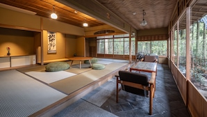A traditional Japanese room with tatami flooring, a wooden ceiling, and large windows offering a view of the forest. - ThinkStay Mt. (Kobe)