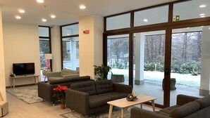 Ein modernes Wohnzimmer mit Fernseher, grauen Sofas, einem kleinen Couchtisch und einem großen Fenster mit Blick auf einen verschneiten Garten.