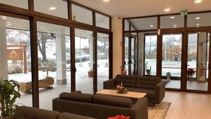 Eine großzügige Lobby mit hohen Glasüren, die nach draußen führen, einem Empfangsbereich und mehreren Sofas.