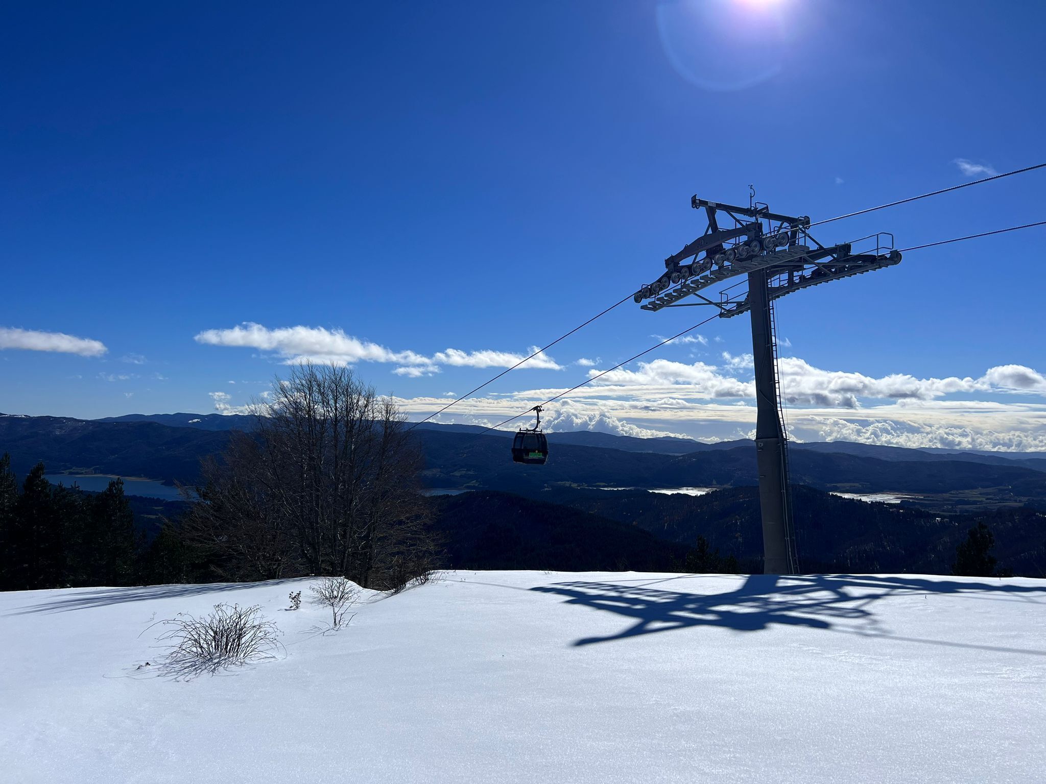 A ski lift with a cable car system, a clear blue sky, and a snowy landscape with distant mountains.