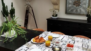 A dining table with a vintage tablecloth, a plate of croissants, glasses of orange juice, and a small bowl of cherries. - Le Clos des Consuls (Tarascon)