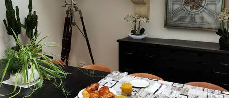 A dining table with a vintage tablecloth, a plate of croissants, glasses of orange juice, and a small bowl of cherries.