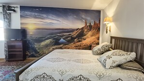 A bedroom with a large bed, a flat-screen TV, a wall-mounted lamp, and a scenic mural of a sunset over a mountainous landscape. - Le Clos des Consuls (Tarascon)