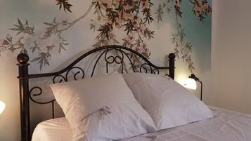 A neatly made bed with white linens and two pillows, a dark metal headboard, and a wall with a floral mural.