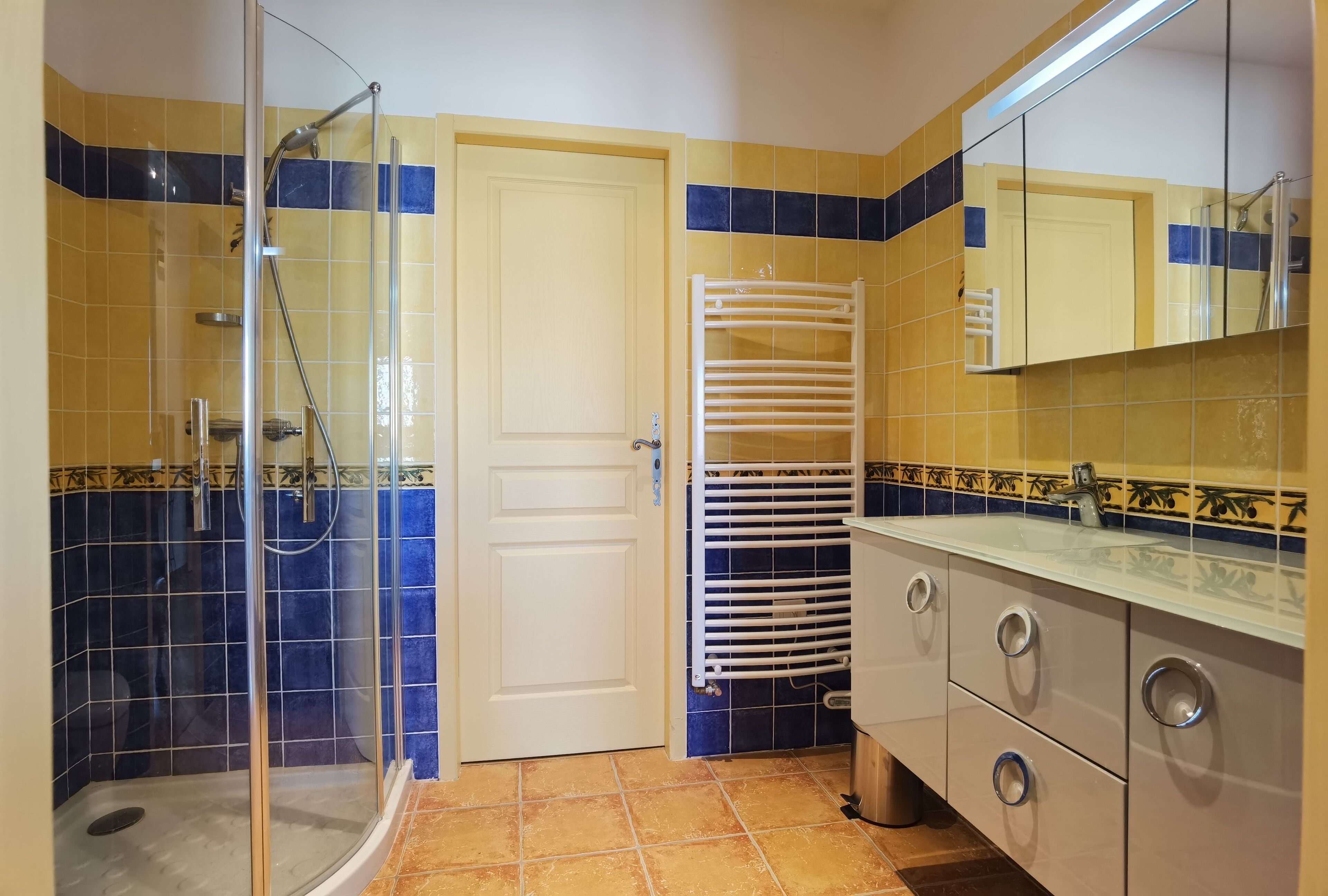 A bathroom with a shower, a white door, and a tiled floor.