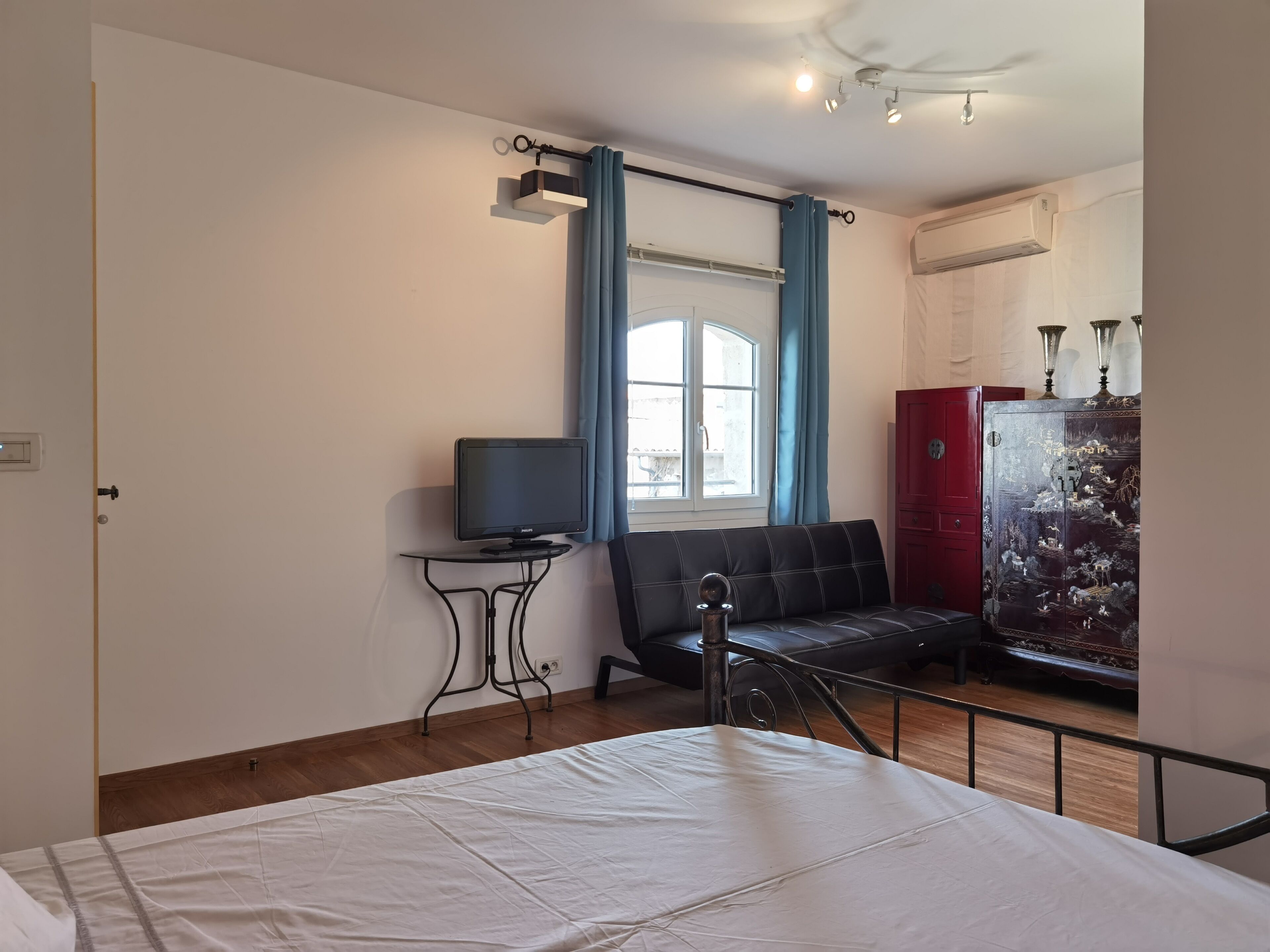 A bedroom with a bed, a TV on a small table, a sofa, and a cabinet with decorative panels.